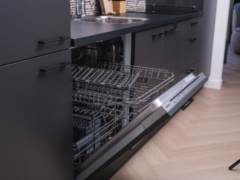 Open dishwasher in a modern lodge kitchen with black cabinets and wooden floor, ready for loading dishes.