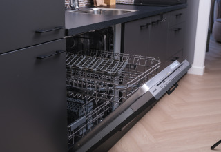 Geöffnete Spülmaschine in einer modernen Lodge-Küche mit dunklen Schränken und Holzfußboden.