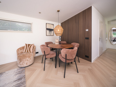 Salle à manger moderne dans un lodge, avec chaises arrondies, table en bois et suspension près d’un mur lambrissé.