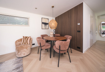 Comedor moderno en una cabaña, con sillas redondas, mesa de madera y lámpara colgante junto a paneles de madera.