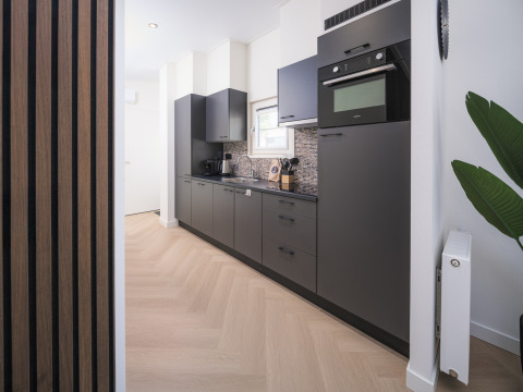 Moderne Lodge-Küche mit schwarzen Schränken, eingebautem Ofen und hellem Holzboden, viel Licht.