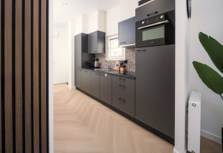 Cuisine moderne de lodge avec armoires noires, four encastré, crédence mosaïque et sol en bois clair.