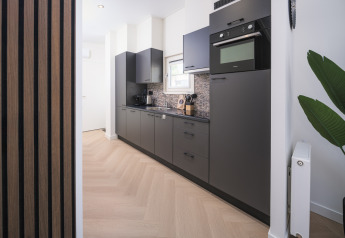 Moderne Lodge-Küche mit schwarzen Schränken, eingebautem Ofen und hellem Holzboden, viel Licht.