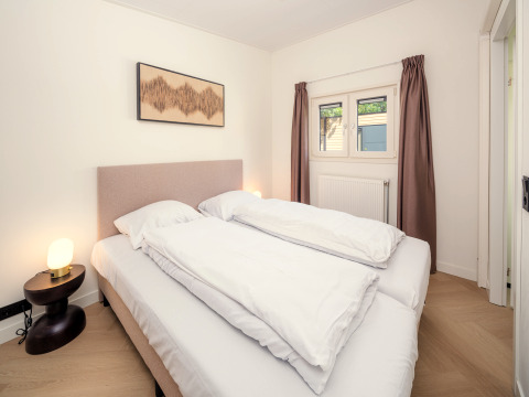 Chambre dans un lodge avec lit double, table de nuit, lampe et rideaux marron aux fenêtres.