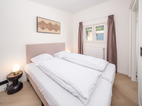 Schlafzimmer in einer Lodge mit Doppelbett, Nachttisch und Lampe, Fenster mit braunen Vorhängen.