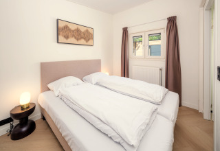 Chambre dans un lodge avec lit double, table de nuit, lampe et rideaux marron aux fenêtres.
