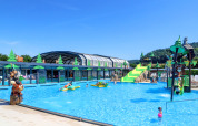 Piscina all'aperto con scivoli per bambini e statue di animali al Camping Nommerlayen, Lussemburgo, in una giornata di sole.