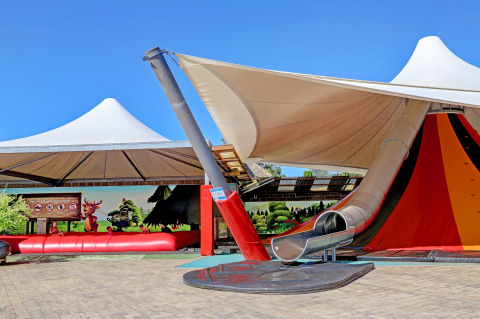 Aire de jeux avec toboggan et auvent au Camping Nommerlayen, Luxembourg, sous un ciel bleu clair.