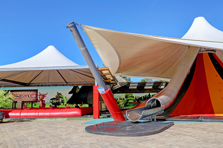 Parque infantil con tobogán y toldo solar en Camping Nommerlayen, Luxemburgo, cielo azul claro.