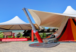 Playground with slide and sun canopy at Camping Nommerlayen holiday park in Luxembourg, clear blue sky.