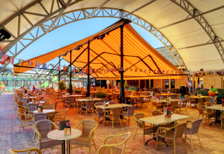 Area pranzo all'aperto con tavoli e sedie sotto tenda a strisce a Camping Nommerlayen, Lussemburgo.