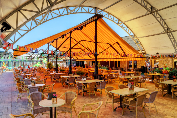 Buitenruimte met tafels en stoelen onder gekleurde luifel bij Camping Nommerlayen, Luxemburg.