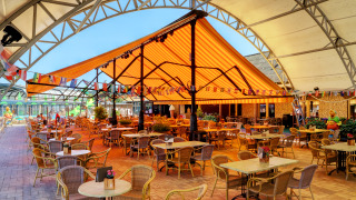 Outdoor dining area with tables and chairs under a striped canopy at Camping Nommerlayen, Luxembourg.