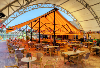 Outdoor dining area with tables and chairs under a striped canopy at Camping Nommerlayen, Luxembourg.