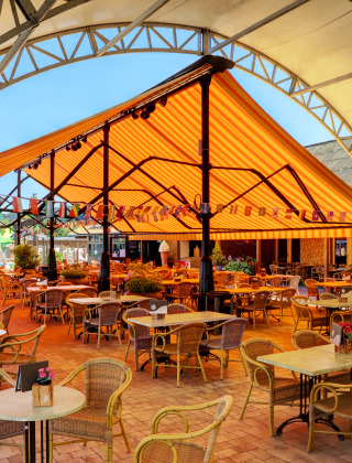 Udendørs spiseområde med stole og borde under farverig markise i Camping Nommerlayen, Luxembourg.