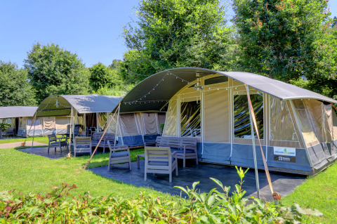 Outdoor view of modern glamping tents with patio furniture and lush greenery at a scenic lodge campsite.