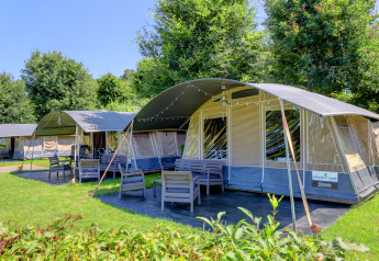 Buitenbeeld van moderne glampingtenten met tuinmeubilair in een groene omgeving bij een gezellige lodge.