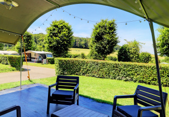 Gezicht vanaf een lodge met terras, stoelen en een groene omheining in een landschap van gras en bomen.