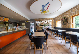 Salle à manger du Camping Nommerlayen au Luxembourg, avec déco moderne, comptoir orange et grandes fenêtres.