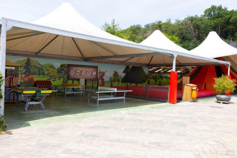 Outdoor play area with tables, colorful mural and tented roof at Camping Nommerlayen in Luxembourg, Luxembourg.