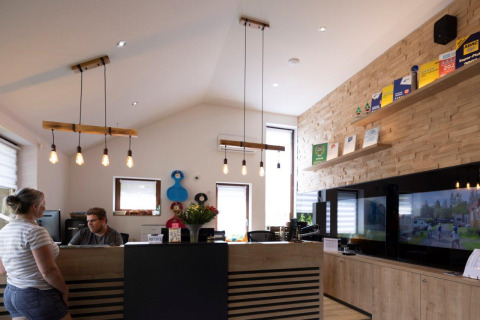Reception area at Camping Nommerlayen holiday park featuring staff, a guest, and modern décor in Luxembourg.