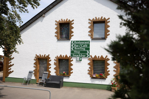 White building with sign pointing to restaurant, bar, café, bowling, shop, and snackbar at Camping Nommerlayen.
