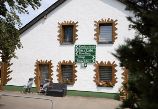 White building with sign pointing to restaurant, bar, café, bowling, shop, and snackbar at Camping Nommerlayen.