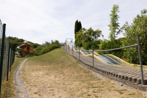 Photo d’un toboggan extérieur et d’une aire de jeux entourés de verdure à Camping Nommerlayen au Luxembourg.