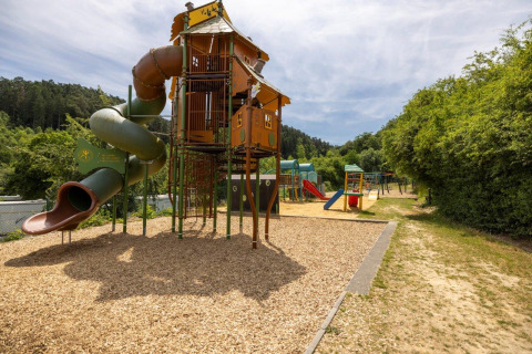 Playground with slide and climbing tower at Camping Nommerlayen in Luxembourg, surrounded by greenery.