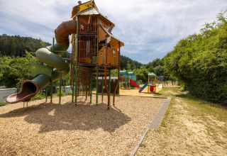 Parco giochi con scivolo e torre da arrampicata al Camping Nommerlayen in Lussemburgo, circondato dal verde.