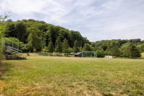 Campo da calcio con tribuna e bosco al Camping Nommerlayen, un villaggio vacanze in Lussemburgo.