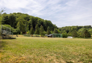 Campo da calcio con tribuna e bosco al Camping Nommerlayen, un villaggio vacanze in Lussemburgo.
