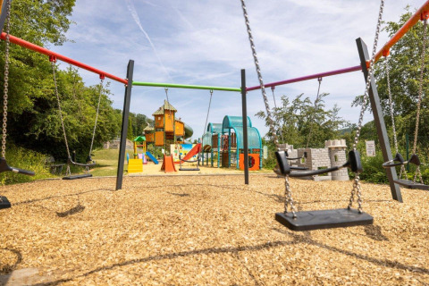 Playground with swings, slides, and climbing frames at Camping Nommerlayen in Luxembourg on a sunny day.