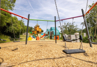 Playground with swings, slides, and climbing frames at Camping Nommerlayen in Luxembourg on a sunny day.