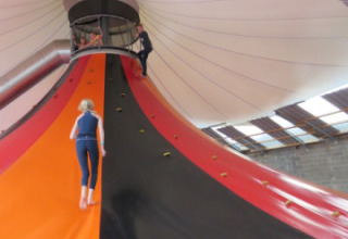 Bambini giocano su uno scivolo vulcano da arrampicata al coperto a Camping Nommerlayen, Lussemburgo, sotto un tendone.