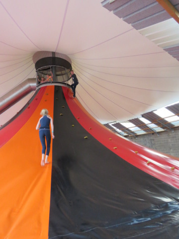 Kinderen spelen op een indoor klimvulkaan-glijbaan in Camping Nommerlayen, Luxemburg, onder een fel doek.