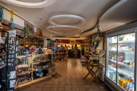 Tienda con estantes, nevera y compradores en Camping Nommerlayen, parque vacacional en Luxemburgo, Luxemburgo.