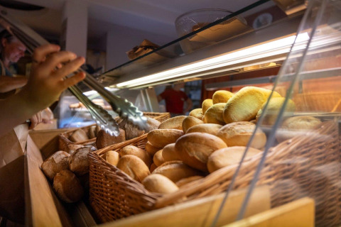Eine Hand greift mit einer Zange frische Brötchen aus einem Korb in der Bäckerei auf Camping Nommerlayen.