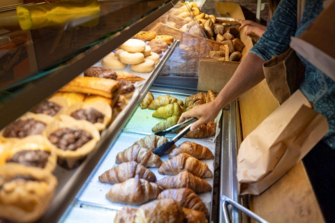 Una persona sceglie croissant e pasticcini freschi dal bancone di Camping Nommerlayen, Lussemburgo.