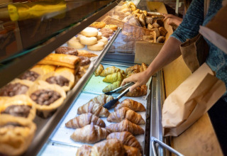Una persona sceglie croissant e pasticcini freschi dal bancone di Camping Nommerlayen, Lussemburgo.