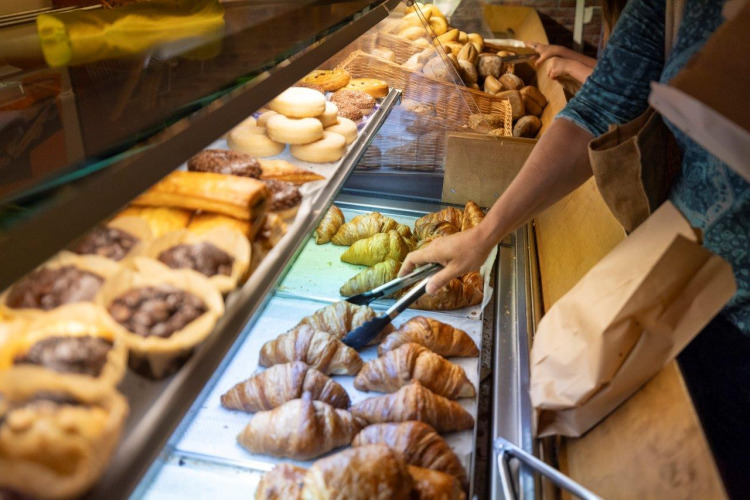 Iemand kiest verse croissants en gebak uit de toonbank bij Camping Nommerlayen in Luxemburg.