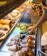 En person vælger friskbagte croissanter og wienerbrød fra et bageriudsalg på Camping Nommerlayen.