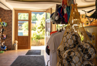 Entrada de una tienda de camping con balones de fútbol en red y ropa en Camping Nommerlayen en Luxemburgo.