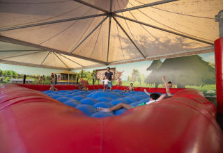 Children play on a large inflatable jumping pillow under a tent at Camping Nommerlayen in Luxembourg.