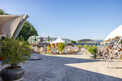 Outdoor seating area at Camping Nommerlayen holiday park in Luxembourg, with pavilions and greenery.