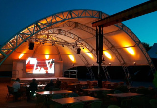 Palco all'aperto con tetto a tenda illuminato di sera al Camping Nommerlayen in Lussemburgo.