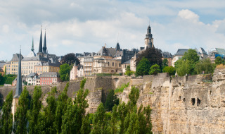 Veduta panoramica della città di Lussemburgo con edifici storici, scogliere e alberi verdi rigogliosi.