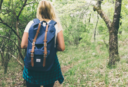 Woman with a backpack walking on a forest trail, ideal image for a glamping holiday park experience.