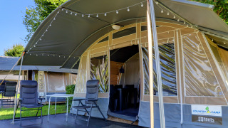 Tente lodge confortable avec chaises et guirlande lumineuse, idéale pour une expérience glamping en pleine nature.