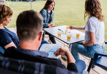Vier personen zitten samen aan een tafel in een lodge, drinken sap en spelen een gezelschapsspel.